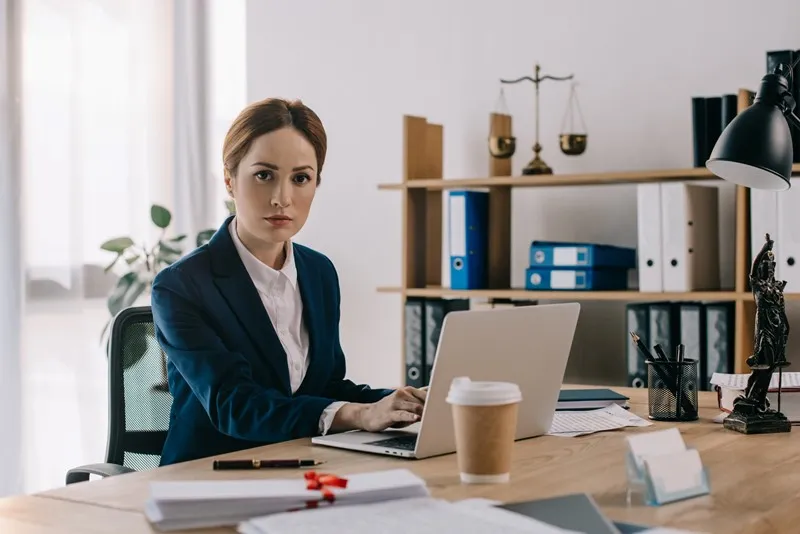 Adviseur achter haar macbook in blauwe blazer met haar koffie to go