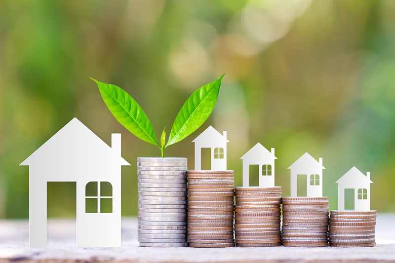 Huisjes die zijn geknipt op een stapel van euro muntjes waaruit vervolgens een plantje groeit